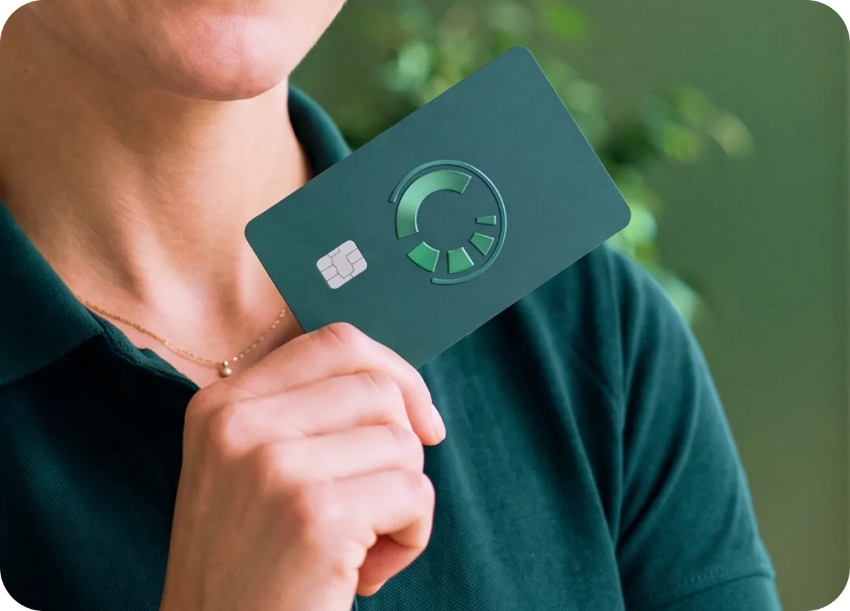 A person holding a dark green credit-builder card over their shoulder.